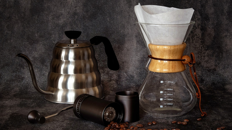 A metal, gooseneck kettle next to a glass pour over coffee maker with whole beans in foreground