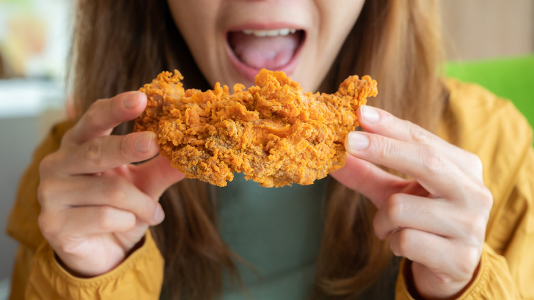 A woman biting into a piece of fried chicken