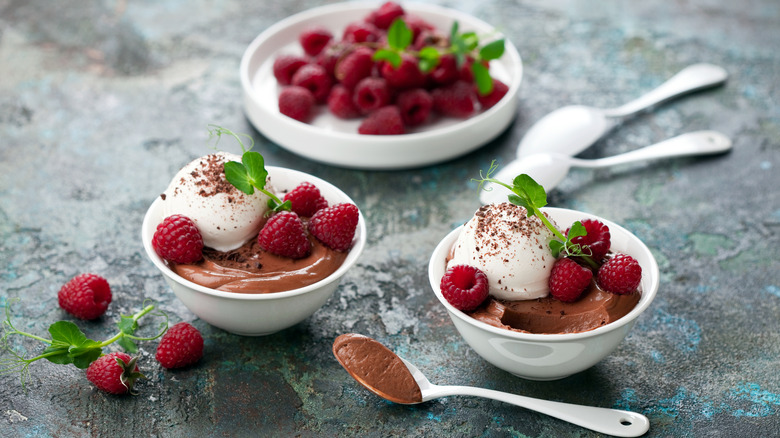 Chocolate mouse with vanilla ice cream and raspberries in white bowls and spoons