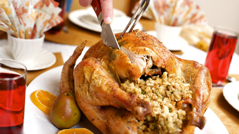 Whole Thanksgiving turkey with stuffing inside being carved with knife