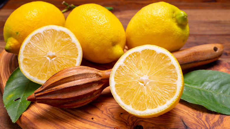 Fresh lemons with squeezer on wooden board