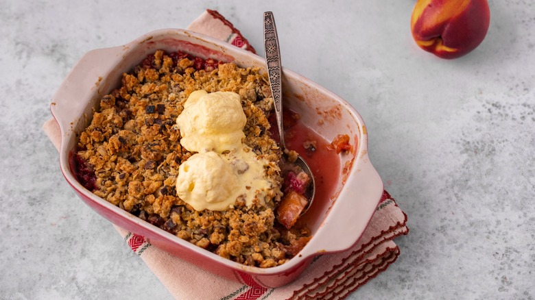 Peach cobbler topped with ice cream on a cloth mat next to a peach