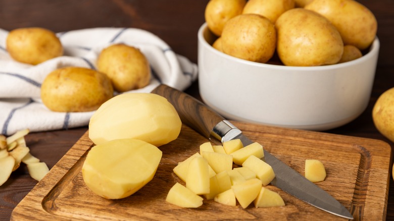 Whole and sliced potatoes on a wooden board with knife