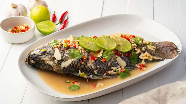 Steamed whole fish on a plate with chilies, lime, and garlic