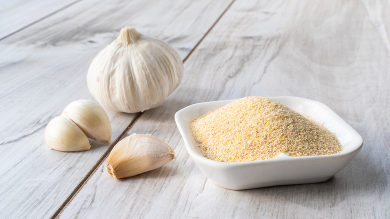 Garlic cloves next to a bowl of garlic powder