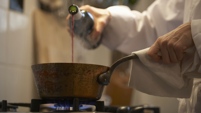 Cook pouring red wine into sauce pan