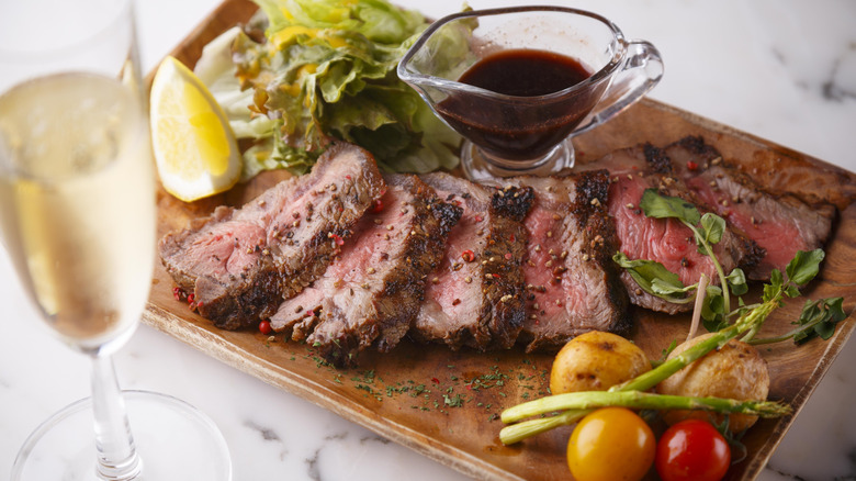 Slices of steak on a wooden cutting board with a boat of wine sauce