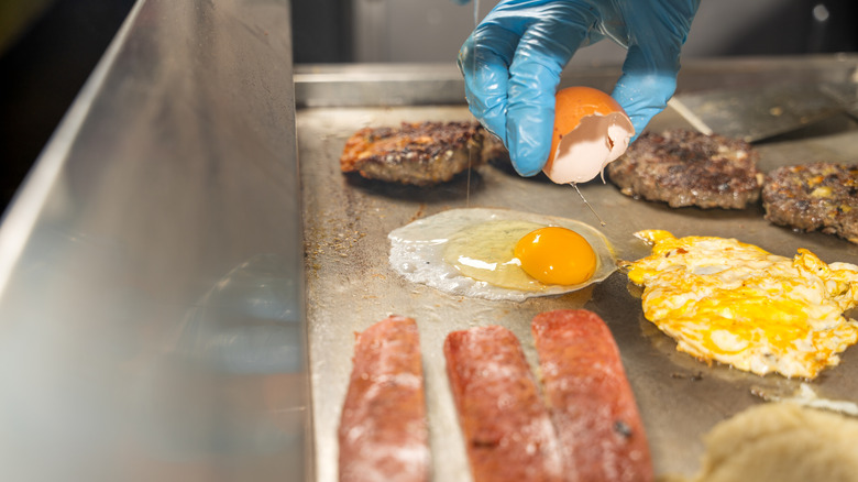 Chef cracking an egg onto a loaded griddle