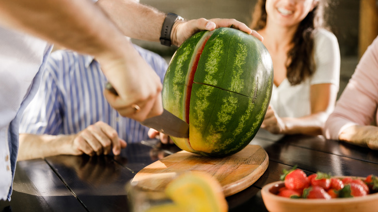 Person cutting watermelon with large knife