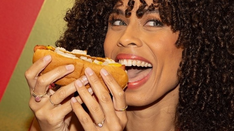 Woman holding American Coney Island hot dog and smiling