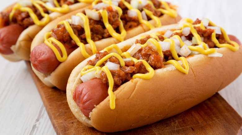 Coney hot dogs with chili, onions, and mustard on wood board