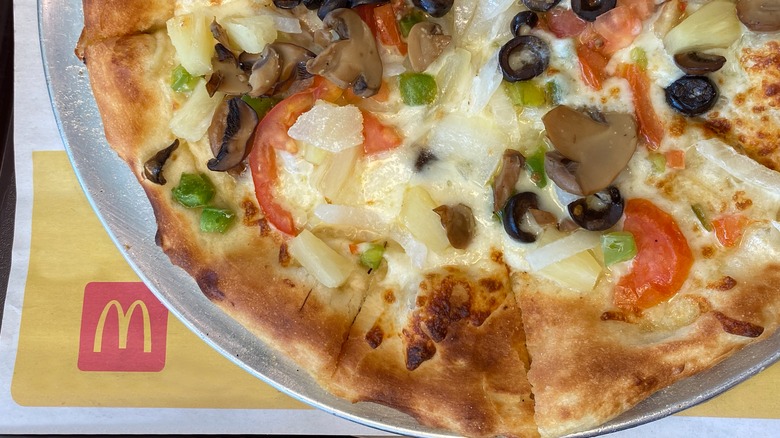 McDonald's pizza topped with mushrooms, tomatoes, green peppers, pineapple, and cheese sits on a paper bearing the McDonald's logo