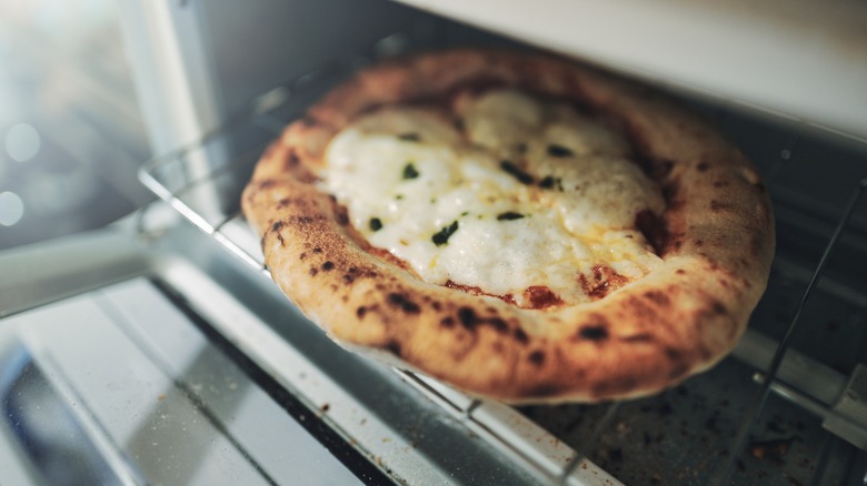 A small pizza being heated in a toaster oven