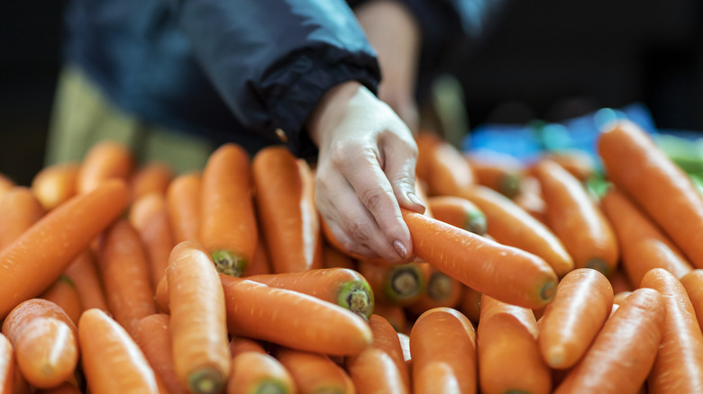 Person in the grocery store reaches for a whole carrot