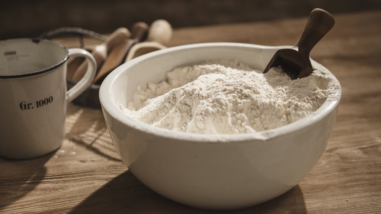 bowl of flour on a wooden table with kitchen utensils in a basket at the back