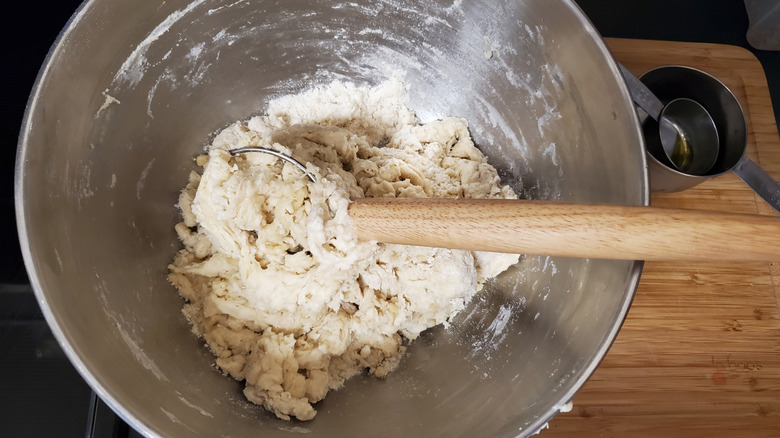 A Danish dough whisk in a stainless steel bowl of bread dough next to measuring cups