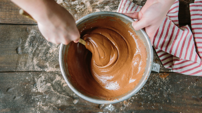 A person stirs a stainless steel bowl of chocolate batter