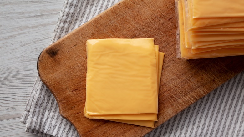 A stack of yellow American cheese slices sit on top of a wooden cutting board