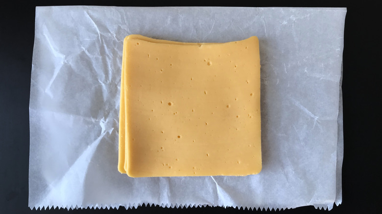 A slice of yellow American cheese on white deli paper and a black background