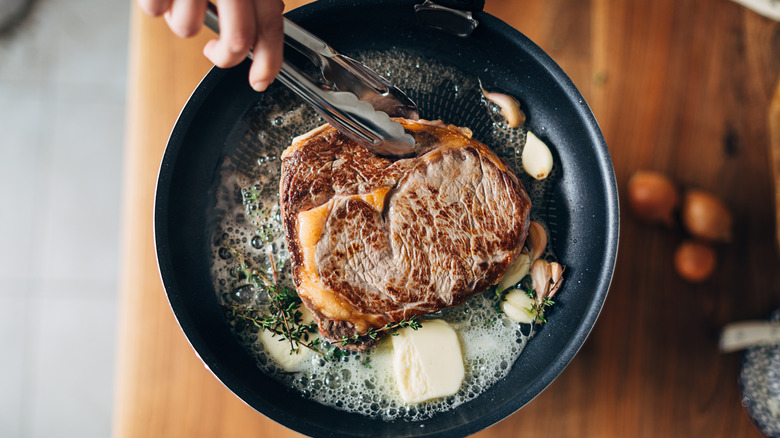 Cooking a marbled ribeye steak in a pan with butter