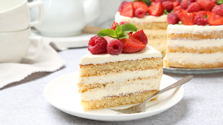 A slice of layer cake with strawberries on top in front of the whole cake.