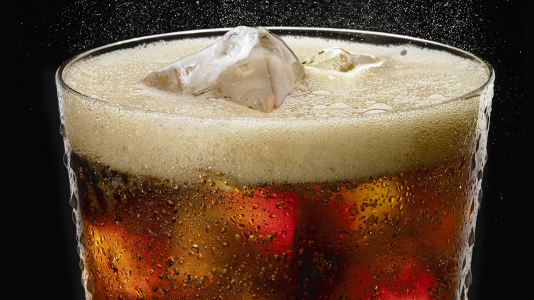 A glass of carbonated soda is shown in closeup with ice.