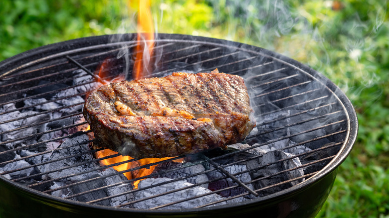 A thick steak on a flaming, charcoal grill