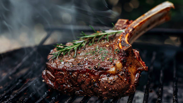 A tomahawk ribeye on the grill garnished with a sprig of rosemary