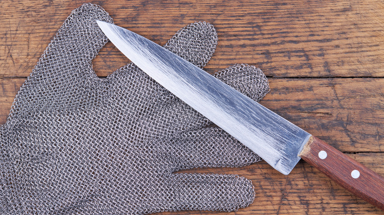 Chainmail metal glove and chef's knife on wood