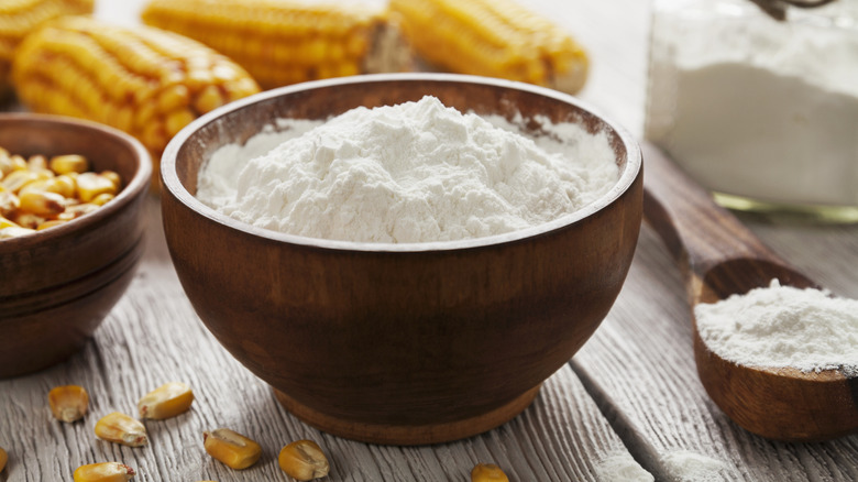 Wooden bowl of cornstarch in a bowl with corn kernels and whole corn cob in the background