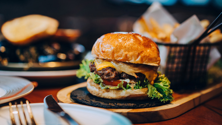 Burger on a wooden serving platter with fries on a restaurant table.