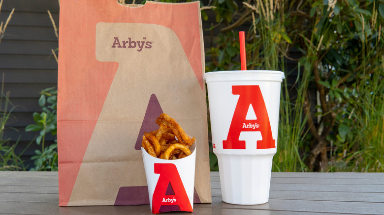 An Arby's takeout bag with a small curly fry and a large drink