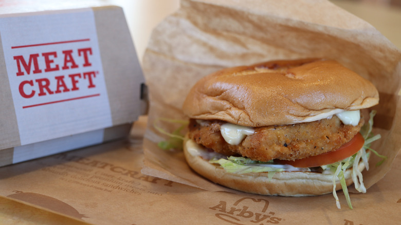 An Arby's chicken sandwich sits on printed Arby's parchment paper