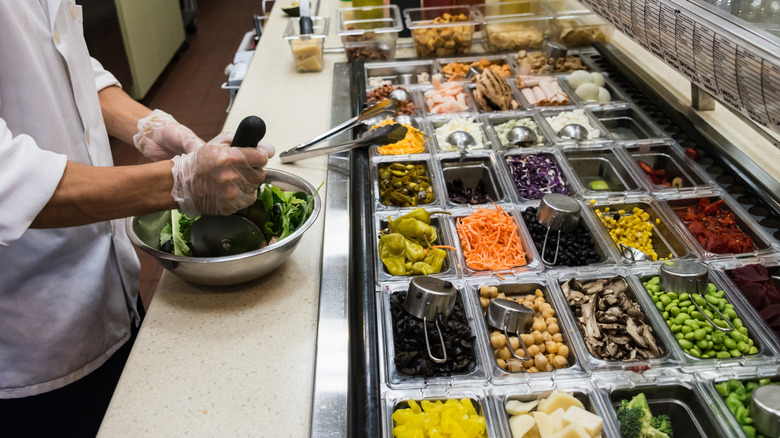 Close up picture of a chef preparing a stainless steel bowl full of assorted salad with salad ingredients