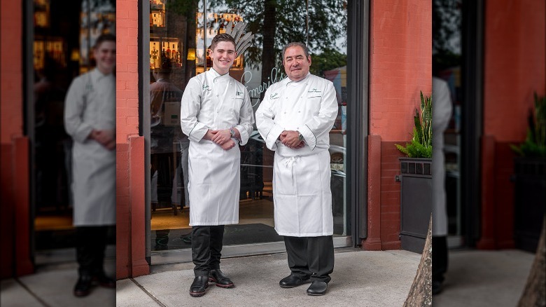 Emeril and EJ Lagasse smiling in front of restaurant