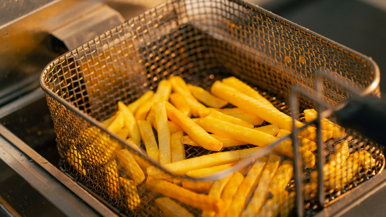 A fry basket holding french fries is lifted from the oil in a restaurant fryer