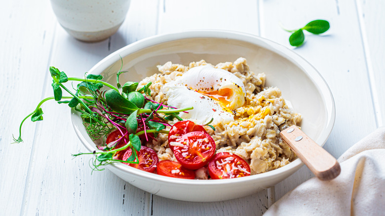 Bowl of oatmeal with tomatoes, herbs, poached egg