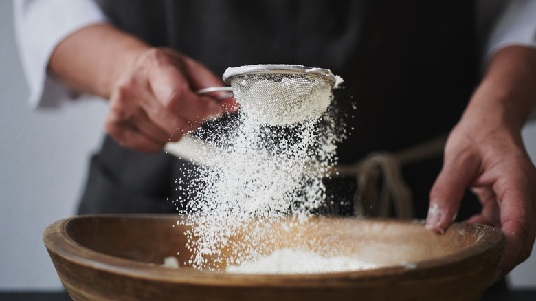 sifting flour into wooden bowl