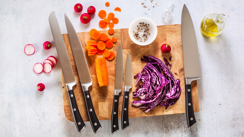 Set of kitchen knives on cutting board with sliced vegetables