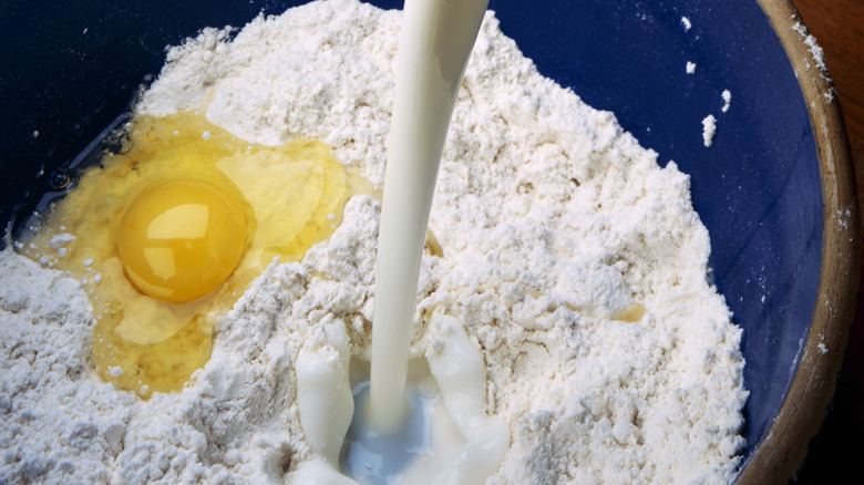 Pouring buttermilk into a bowl of flour with an egg cracked inside