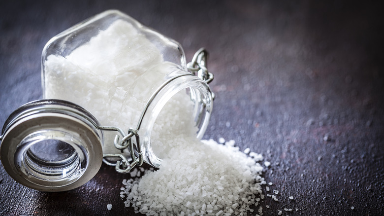 A container of flaky salt rests on its side with salt having poured out of it