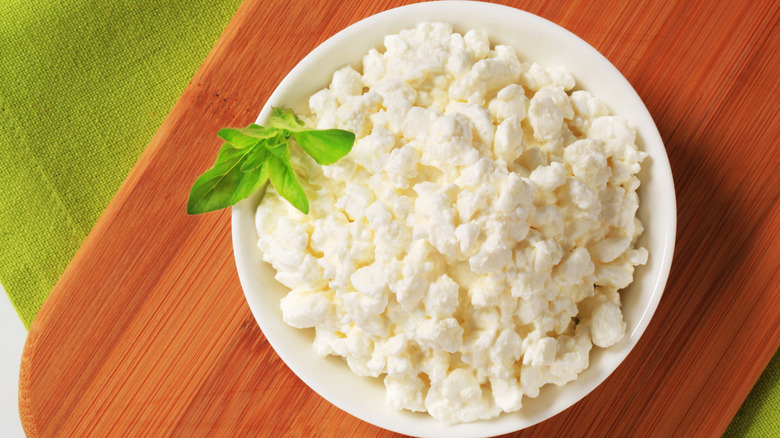 Cottage cheese in a white bowl on a cutting board