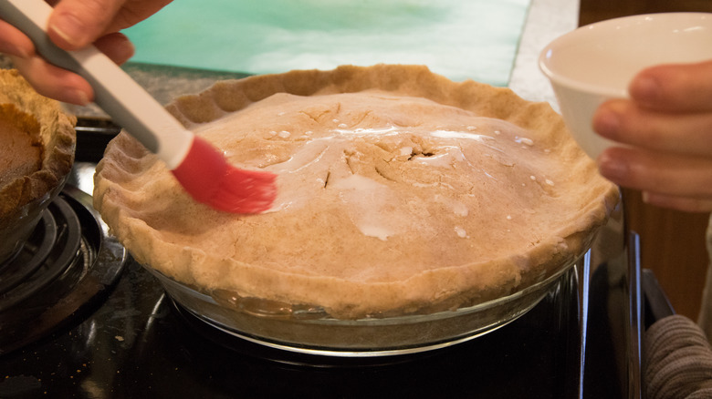 Person brushing cream on raw pie crust