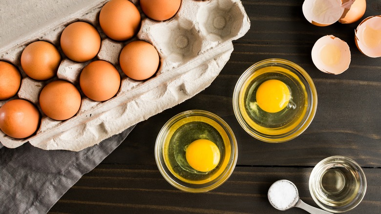 Eggs in carton and cracked into two glass bowls