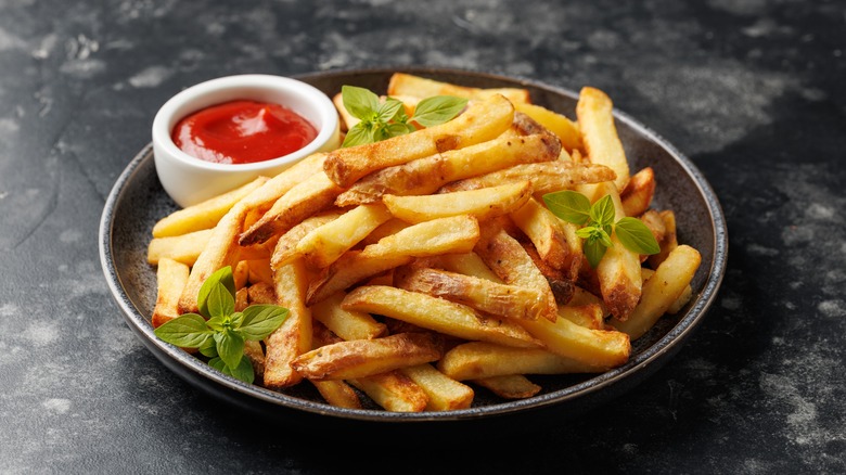 Homemade french fries on a plate sit next to a small ramekin of ketchup