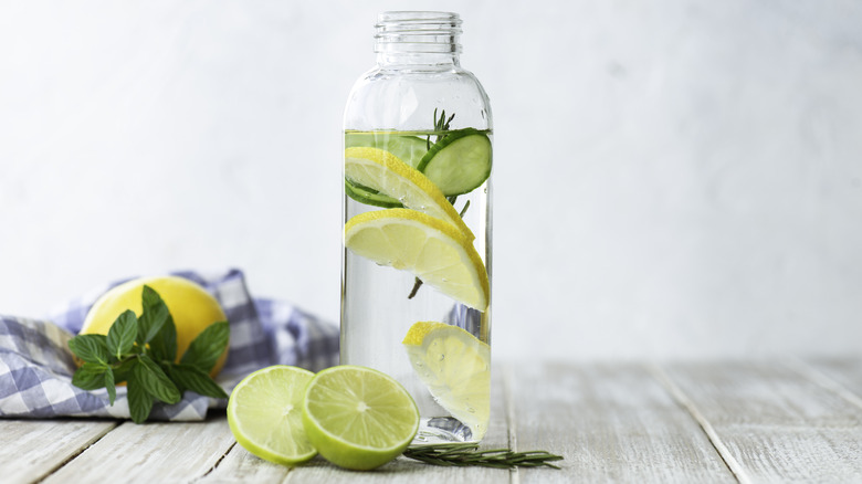 glass bottle filled with water, lemon slices, cucumber slices, and rosemary on a wooden table