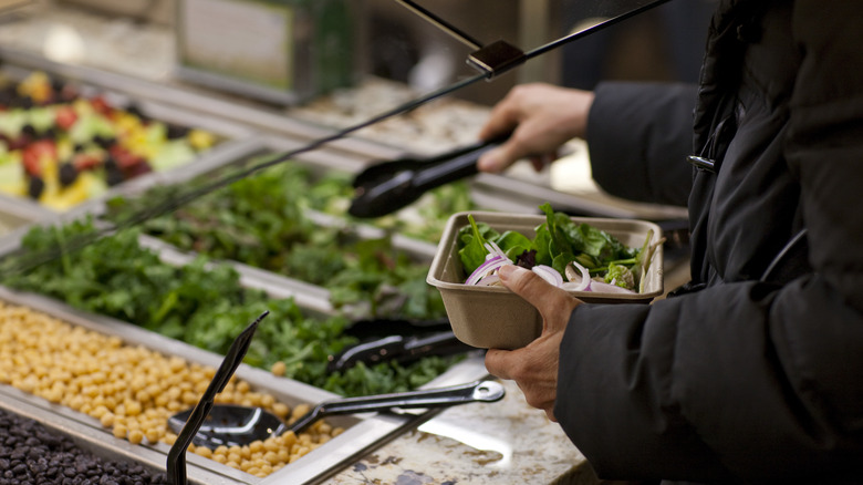 A person filling a food container at a Whole Foods salad bar