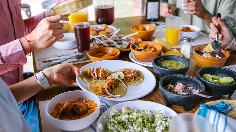 Group of people eating with hands passing a plate over a table full of Mexican food