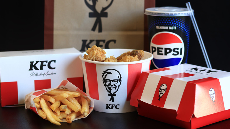 A selection of food from a KFC including a Pepsi drink, a bucket of chicken, fries, and two boxes of food