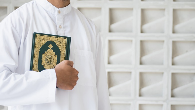a man in white holding a Qur'an holy book